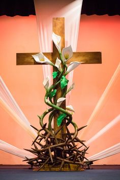 a cross on top of a wooden structure with vines growing out of it and white flowers in the center