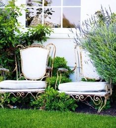 two white chairs sitting next to each other in front of a window on top of green grass