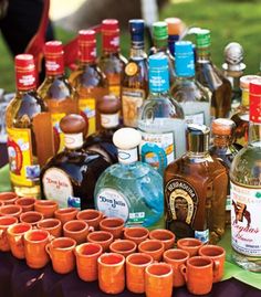 there are many bottles and glasses on the table with cups in front of each one