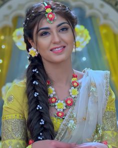 a woman with long hair and flowers in her hair wearing a yellow dress smiling at the camera