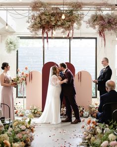 a bride and groom kiss as they stand in front of an arch decorated with flowers