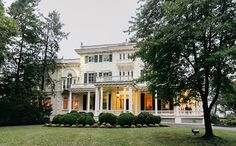 a large white house sitting in the middle of a lush green field next to trees