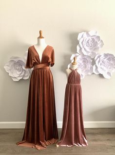 two dresses on mannequins in front of a wall with white paper flowers