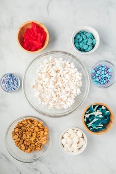 bowls filled with different colored candies and marshmallows on a marble surface