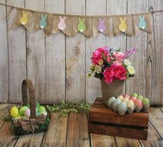 an arrangement of flowers, eggs and bunnies on a wooden table next to a fence