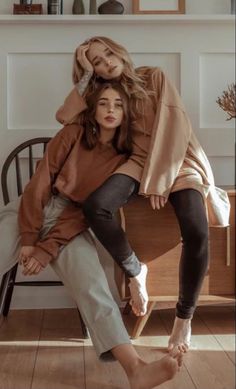 two women sitting on top of each other in the middle of a wooden floored room