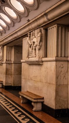 the interior of a train station with benches and sculptures on the wall, along with lights