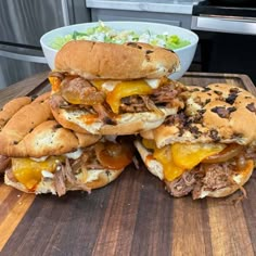 a pile of sandwiches sitting on top of a wooden cutting board next to a bowl of salad