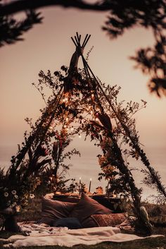 a teepee is set up with lights and pillows on the grass by the water