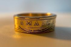 This Jamaican Coin Ring is derived from an authentic 1940's Jamaican (Dates Vary/Same Design/Coin) One Penny Brass Coin. This coin ring is a great statement piece to show your love and appreciation for Jamaica! The effort I place in the ring is made to protect and transfer the details from the coin to the ring. I have personally achieved the coin ring using hand made methods which includes holing the coin, pressing the coin to achieve a cone shape. Then using a Swedish wrap in order to ensure a Vintage Engraved Round Ring Collectible, Vintage Stamped Engraved Ring For Formal Occasions, Vintage Engraved Ring For Formal Occasions, Vintage Round Band Rings For Gifts, Vintage Round Band Engraved Ring For Gift, Vintage Round Band Engraved Ring Gift, Vintage Engraved Round Band Ring As Gift, Formal Vintage Engraved Stamped Ring, Vintage Stamped Rings For Formal Occasions