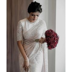 a woman in a white sari holding a bouquet of flowers and looking down at the floor