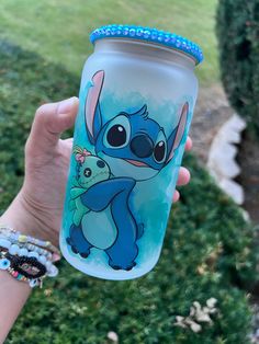 someone holding up a cup with stitching on it in front of some grass and bushes