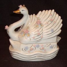 a ceramic swan figurine with flowers on it's tail sitting on a black surface