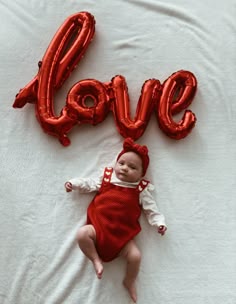 Small Baby girl laying on a white blanket wearing a red and white romper and a red baby bow with a balloon foil spelling the word love for Valentine’s Day photoshoot Valentines Day Newborn Pictures, Valentines Baby Photoshoot Ideas, Valentines Day Newborn Photoshoot, Newborn Baby Valentines Photoshoot, Valentines Pictures Baby, Valentines Baby Pictures, 1 Month Old Baby Pictures Valentines, Infant Valentine Pictures