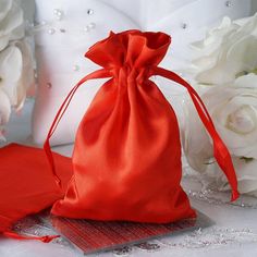 a red satin bag sitting on top of a table next to white flowers