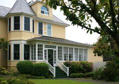 a large yellow house with white trim on the front and side windows, surrounded by greenery