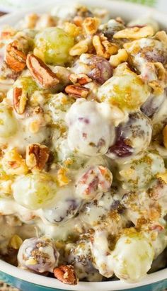 a white bowl filled with grapes and nuts covered in cream cheese sauce on top of a blue table cloth