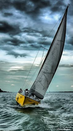 a yellow sailboat in the middle of the ocean under a cloudy sky with dark clouds