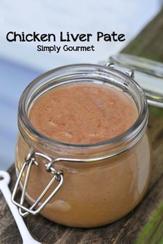 a jar filled with chicken liver pate sitting on top of a wooden table next to a spoon