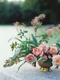 a vase filled with pink flowers sitting on top of a cement slab next to water