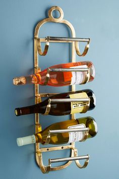 a metal wine rack holding several bottles of wine on a blue wall with a gold finish