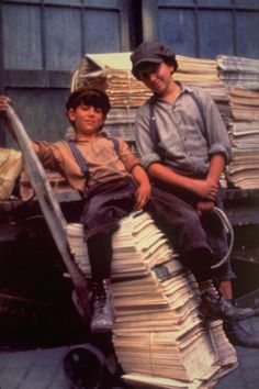 two boys sitting on top of stacks of papers