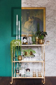 a shelf with candles, plants and bottles on it in front of a green wall