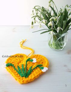 a crocheted heart with flowers in the center on a table next to a vase