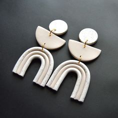 two pairs of white and gold earrings on a black surface, with one pair dangling from the back