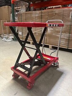 a red scissor sitting on top of a dolly in a warehouse with pallets