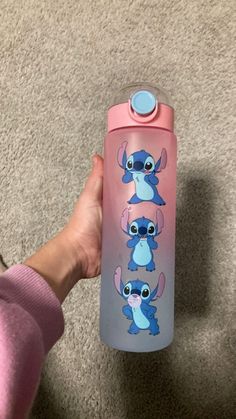 a person holding a pink and blue water bottle with stitching on the side, in front of a carpeted area