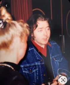 a man in a denim jacket talking to another person