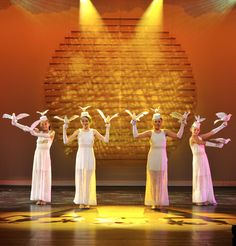 four women in white dresses are performing on stage