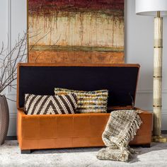 a brown leather bench with pillows on it in front of a painting and floor lamp