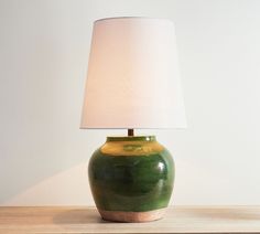 a green vase sitting on top of a wooden table next to a white lampshade