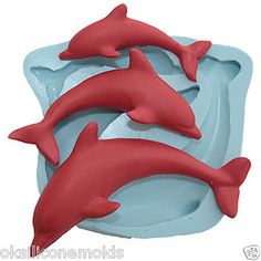 two red dolphins are swimming in the blue water and one is jumping out of the water