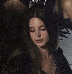 a woman with long hair is looking down at her cell phone while sitting in the dark