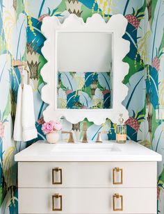 a white dresser topped with a mirror next to a flower covered wallpapered bathroom