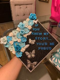 a graduation cap decorated with blue flowers and butterflies is being held up by someone's hand