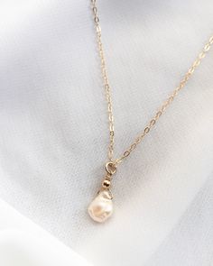 Classic and minimalist, a beautiful freshwater Keshi pearl hangs from our signature thin cable chain. With its organic shape and gorgeous luster, no two pearls are the same. Color ranges from cream and off-white to champagne. This dainty single pearl necklace is handcrafted in Gold Filled or Sterling Silver. Wear alone or layer with your favorite everyday necklaces. Our model is wearing the 16" length necklace. Features: Single Freshwater Keshi Pearl (Approximately 7mm to 10mm In Size) Delicate Pearl Minimalist Necklace, Perl Neckles Simple, Minimalist Gold Necklace With Pearl Drop, Minimalist Gold Pendant Pearl Necklace, Gold Feminine Pearl Pendant Necklace, Luxury Minimalist Pearl Pendant Necklace, Minimalist 14k Gold-filled Pearl Pendant Necklace, Minimal Choker, Gold Drop Necklace