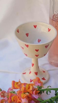 a white bowl with hearts painted on it next to flowers and a pink glass vase