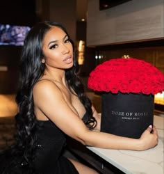 a woman is holding a large black box with red roses in it and posing for the camera