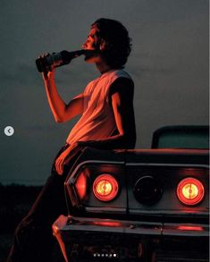 a man sitting on top of a car drinking from a bottle