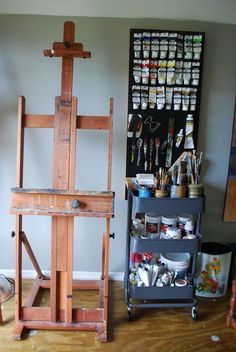 a wooden easel sitting in front of a wall filled with paint and other art supplies