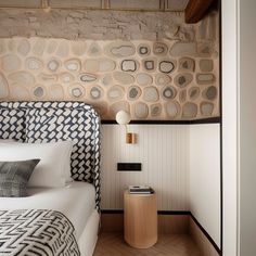 a bed sitting next to a stone wall in a room with wood flooring and white walls