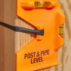 an orange post and pipe level attached to a wooden wall with a screwdriver