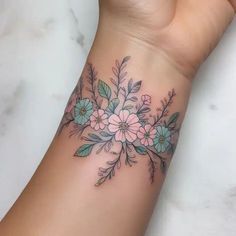 a woman's wrist tattoo with flowers and leaves on the left side of her arm