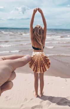 a woman standing on top of a sandy beach next to the ocean holding a shell