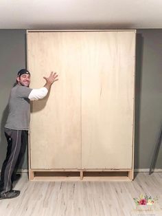 a man standing in front of a wooden cabinet with his hands out to the side