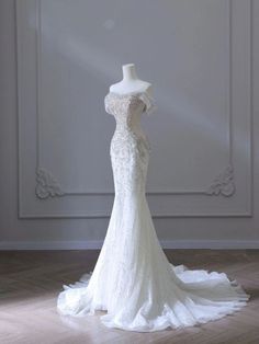 the back of a wedding dress on display in front of a white wall and wooden floor